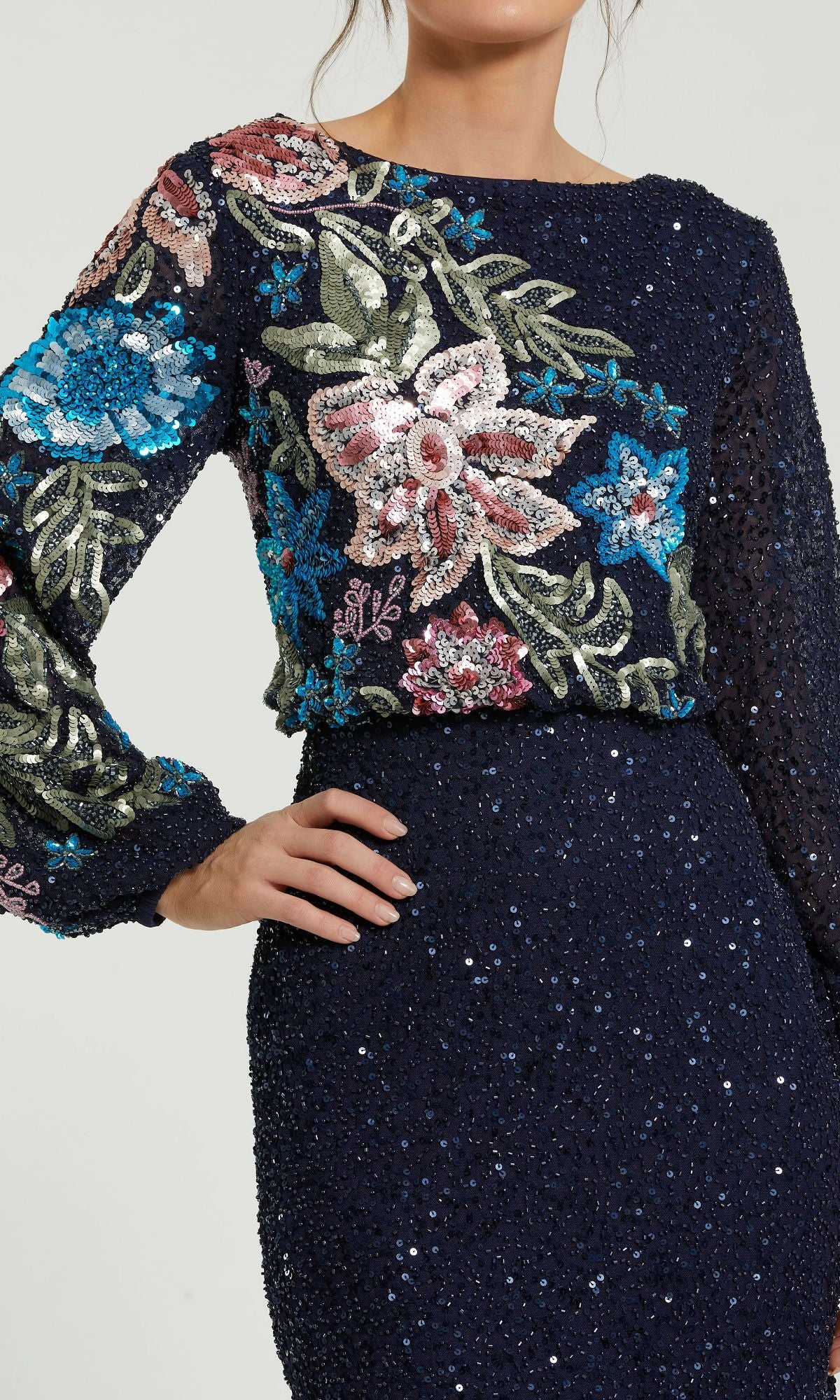 A woman wearing the Mac Duggal 5615 Beaded Long Sleeve Formal Dress, featuring navy blue sequins and colorful floral embroidery on the bodice.